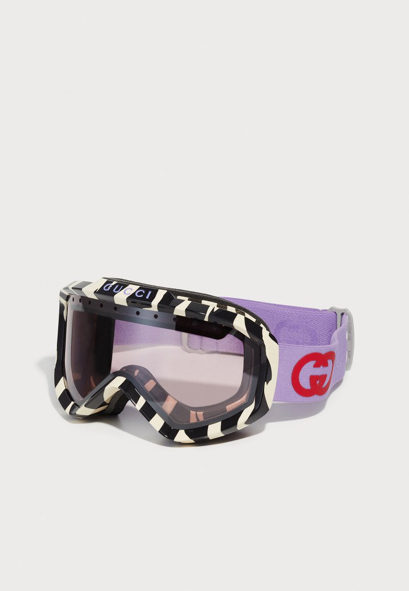 Occhiali da sci Gucci con un telaio a righe bianche e nere, fascia elastica viola con logo rosso e lenti oscurate.