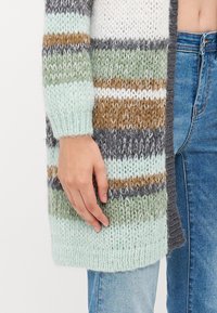 Πλεκτό cardigan με ρίγες σε αχάτη, πράσινο, καφέ, γκρι και λευκό. Έχει υφή, χαλαρή εφαρμογή με ριμπ μανσέτες και ανοιχτό μπροστινό σχέδιο.