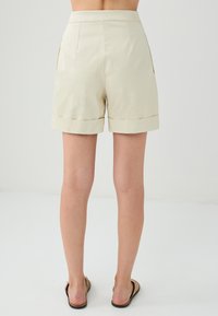 Shorts couleur crème avec un ourlet replié, dotés de poches latérales et d'une texture de tissu lisse. Conçus avec une coupe ajustée et une taille haute.