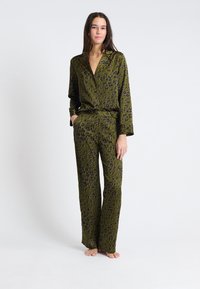 Olijfgroen pyjama set van gladde stof met een bloemenpatroon in paars en zwart. Lange mouwen en losvallende broek met zakken.