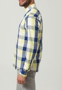 Camicia a maniche lunghe a scacchi caratterizzata da grandi quadrati gialli, verdi e blu. Realizzata in tessuto leggero con polsini a bottoni e colletto classico.