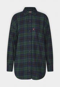 Grünes und marineblaues Karo-Flanellhemd mit langen Ärmeln, einer Knopfleiste, einem spitzen Kragen und einem Logo-Patch auf der linken Brust. Weicher Stoff.