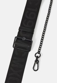 Ceinture en tissu noire avec texte embossé, boucle métallique carrée et chaîne noire amovible avec mousqueton sur fond blanc.