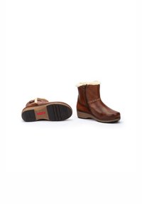 Botas de tobillo de cuero marrón con forro de piel sintética y cremallera lateral. Suela de goma texturizada con un tacón de cuña ligeramente texturizado.