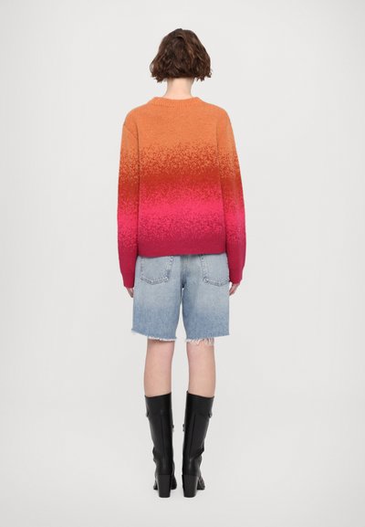 Sweter ma gradient od pomarańczowego do różowego, prążkowany dekolt i mankiety. Połączony z postrzępionymi dżinsowymi szortami i czarnymi wysokimi na kolana botkami.