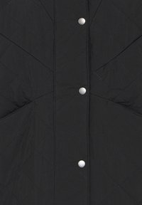 Tela negra acolchada con costura en forma de diamante, con tres botones a presión redondos plateados visibles alineados verticalmente.