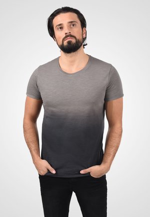 Majica s kratkim rukavima, siva do crna gradijent, okrugli izrez, mekana tekstura, uski kroj, nosi se s rukama u džepovima na svijetloj pozadini.