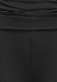 Fekete leggings rugalmas, bordázott anyagból. Magas derékpánttal és sima textúrával rendelkezik; minimális részletezéssel, látható hardver nélkül.