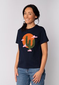 Marineblauwe T-shirt met een cactusafbeelding, roze wolken en een oranje zon. Korte mouwen, ronde halslijn, gemaakt van katoen.