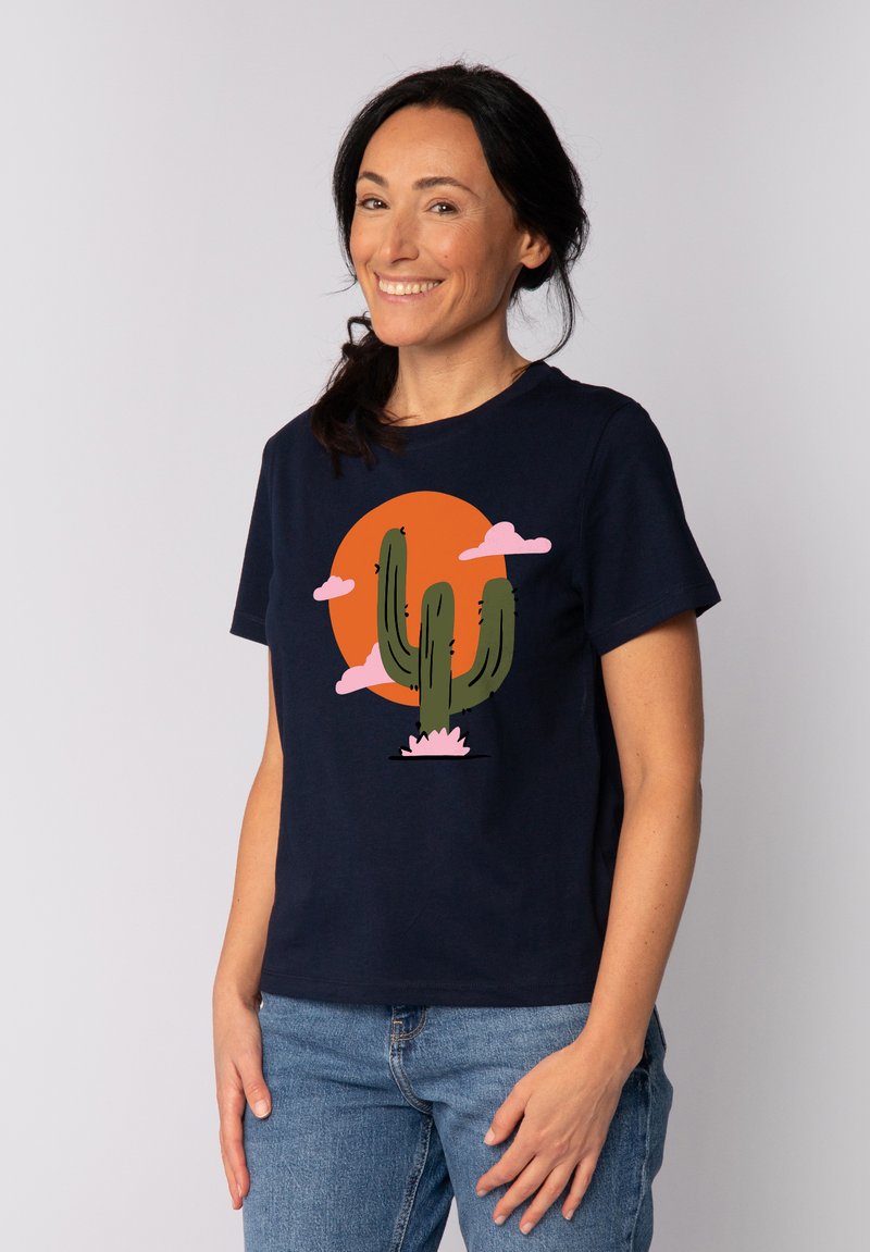 Marineblauwe T-shirt met een cactusafbeelding, roze wolken en een oranje zon. Korte mouwen, ronde halslijn, gemaakt van katoen.