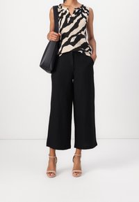 Femme portant un pantalon large noir raccourci, un haut sans manches à imprimé animal beige et noir, des sandales à talons beiges, et un sac à bandoulière noir.