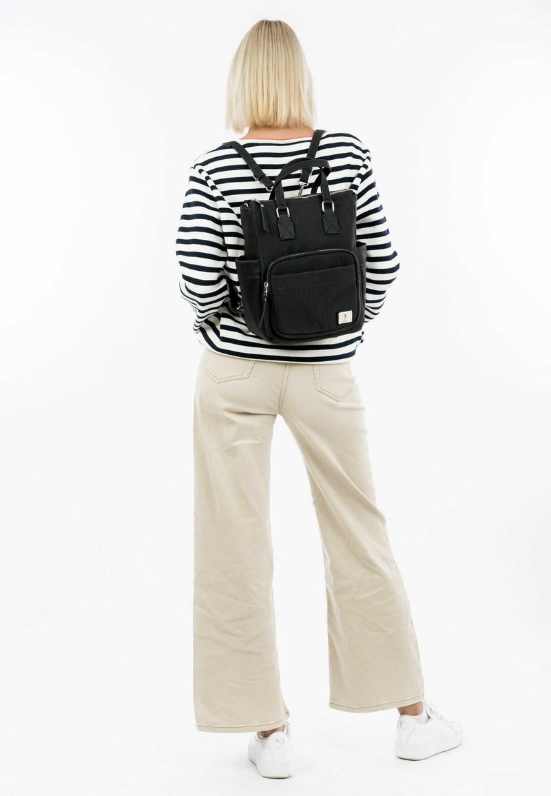 Black fabric backpack with dual top handles, adjustable straps, front zip pocket, and side pockets. Features a subtle textured design.