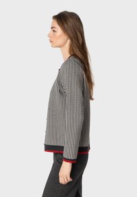 Cardigan grigio e nero a motivo houndstooth con dettagli rossi, lavorazione a maglia testurizzata, scollo rotondo, fronte con bottoni e maniche lunghe.