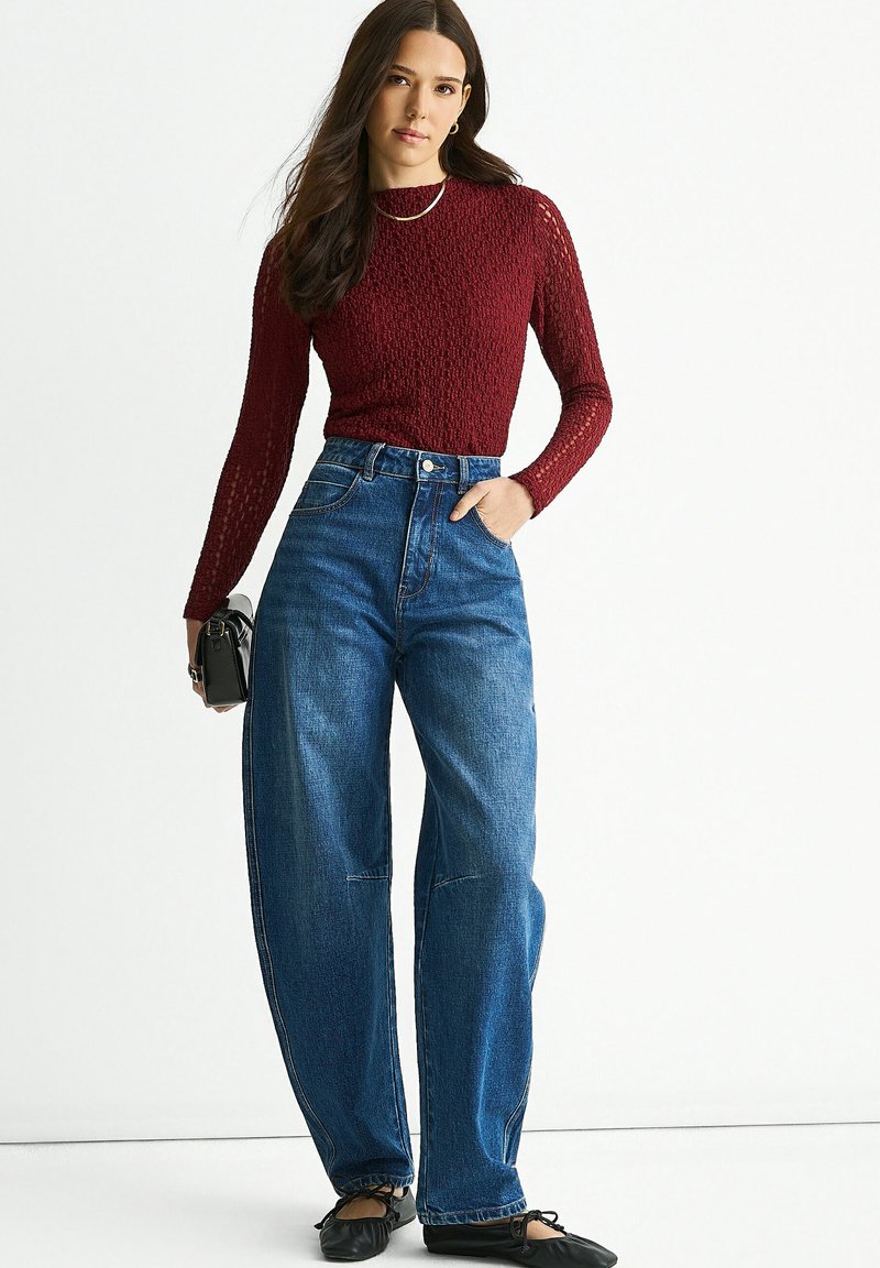 Red textured knit long-sleeve top paired with high-waisted, wide-leg blue denim jeans. Model is holding a small black bag.