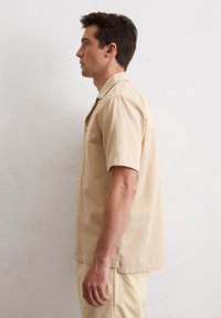 Beige overhemd met korte mouwen en een subtiel textuurpatroon, in een ontspannen pasvorm, gecombineerd met lichtbeige broek.