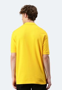 Gelbes Polohemd mit kurzen Ärmeln, glatter Textur und klassischem Kragen. Nahtloses Design mit geradem Schnitt am Rücken.