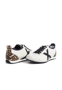 Białe sneakersy z czarnym wzorem w krzyż, z tyłem w nadruk w panterkę. Wykonane ze skóry o teksturowanym wykończeniu. Gumowa podeszwa.