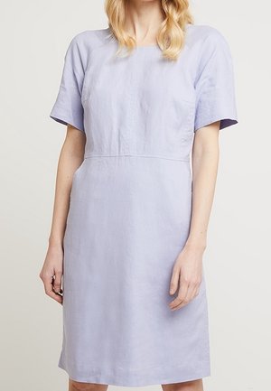 Femme portant une robe courte jusqu'aux genoux, de couleur lavande claire, à manches courtes, avec une silhouette droite et un col rond.