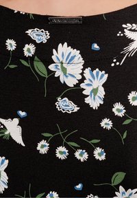 Czarny materiał z białym i niebieskim wzorem kwiatowym, zielonymi liśćmi, małymi niebieskimi sercami oraz metalową metką szytą z napisem "VIVE MARIA".