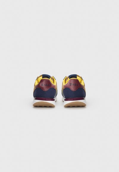 Chaussures de sport multicolores avec des côtés en maille bleu marine, des accents jaunes et un talon texturé avec un logo bordeaux. Semelle en caoutchouc blanche.