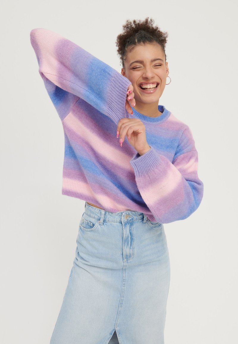 Knitted sweater in pastel pink, purple, and blue stripes; cropped design with wide sleeves. Paired with high-waisted light blue denim skirt.