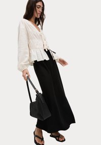 Vit, texturerad blus med peplum-kant och knytframsdetalj, i kombination med en lång svart nederdel. En svart väska och platta sandaler fulländar looken.