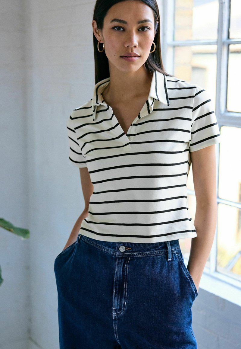 Polo cu dungi în crem și negru, cu guler și mâneci scurte, asortat cu pantaloni din denim bleumarin, prevăzuți cu un nasture și buzunare.