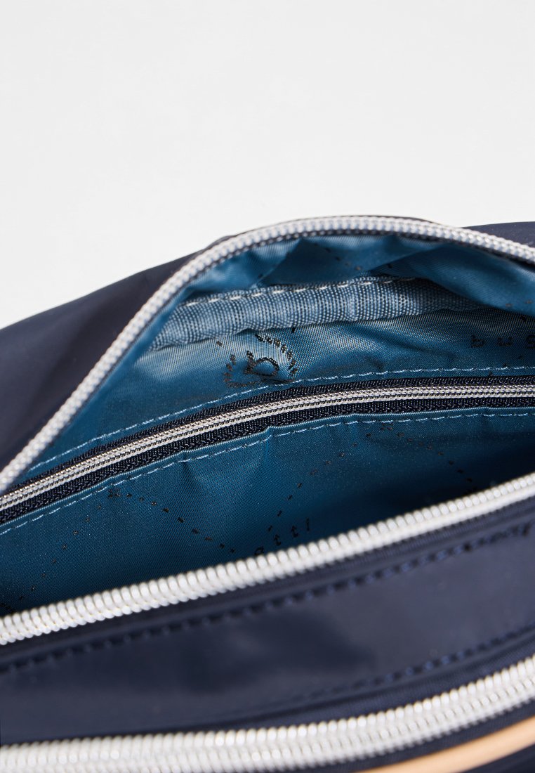 Sac bleu marine avec un extérieur lisse et brillant. L'intérieur présente une doublure bleu clair contrastante, des compartiments zippés et un design structuré.