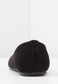 Chausson en suède noir à enfiler avec un profil bas, un bout arrondi et une semelle plate en caoutchouc. Présente des coutures soignées et une texture lisse.