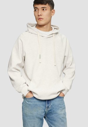 Light beige cotton hoodie with a kangaroo pocket, adjustable drawstrings, and ribbed cuffs, paired with light blue denim jeans.