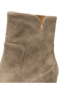 Mockasiner i ljus taupe med en ren, böjd design. Har en mjuk innerfoder och subtila sömnaddetaljer längs kanterna.