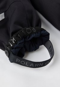 Marineblåt stof med tekstureret overflade, der har en sort justerbar rem mærket "POLARN O." og en knapdetalje på lukningen.