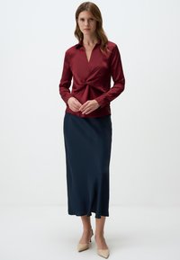 Burgundy satin blouse with a V-neck and twist detail at the front, paired with a sleek navy satin skirt and beige high-heeled shoes.