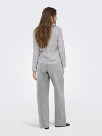 Camicia a righe azzurra e bianca abbinata a jeans grigi a vita alta e a gamba larga. L'outfit presenta una vestibilità rilassata e maniche lunghe.