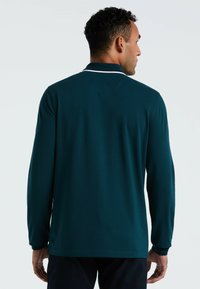 Teal langemouwen polo-shirt met een platte kraag, contrasterende witte afwerking en een gladde textuur. Het shirt heeft een rechte snit en lange mouwen.