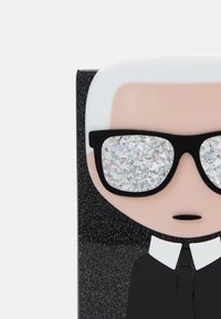 Projekt postaci przedstawiający osobę z białymi włosami w czarnym garniturze, dużymi czarnymi okularami i błyszczącymi srebrnymi szkłami na teksturowanym czarnym tle.