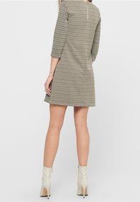 Kostymklänning med hounds-tooth-mönster och trekvartslånga ärmar, strukturerad form, dragkedja bak, kombinerad med vita ankelskor.