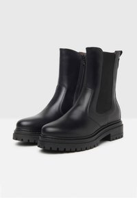 Bottines en cuir noir avec une finition lisse, des panneaux latéraux élastiques, une fermeture éclair et une semelle en caoutchouc texturée et épaisse.