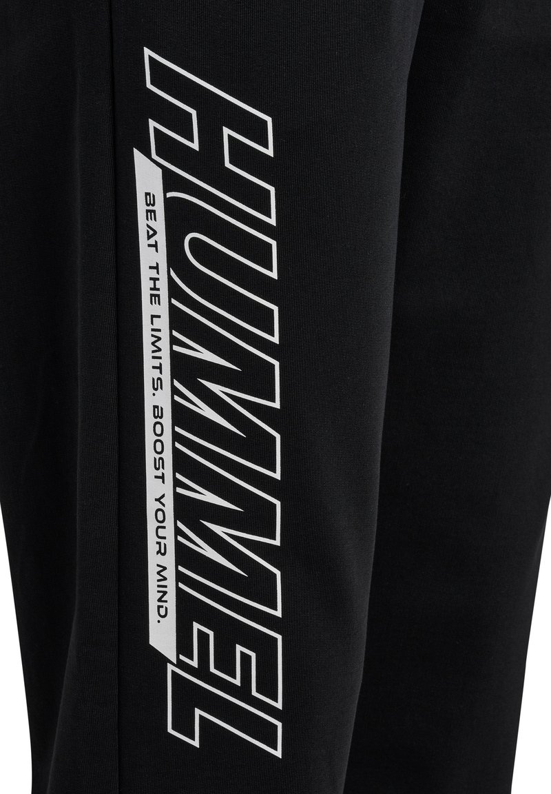 Czarne spodnie dresowe wykonane z miękkiego materiału, z wyraźnym białym logo i napisem biegnącym wzdłuż nogawki, o gładkiej teksturze i tapered designie.