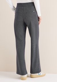 Szare spodnie o szerokich nogawkach wykonane z teksturowanego dzianego materiału, z dwoma tylnymi kieszeniami i paskiem w talii. Połączone z beżowym obuwiem z niebieskimi akcentami.