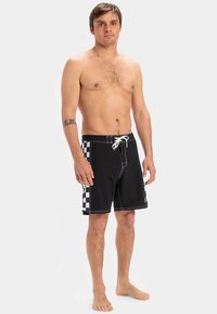 Čierne šortky na pláž s károvaným vzorom na ľavej strane, bielym prešívaním a elastickým pásom s bielym šnúrkou na stiahnutie.