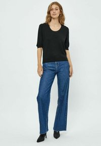 Černý pletený top s krátkými rukávy, kombinovaný s džínami světle modré barvy se širokými nohavicemi a vysokým pasem. Outfit doplňují černé lodičky s špičatou špičkou.
