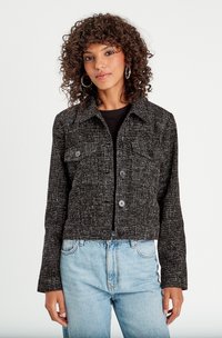 Giacca cropped in tweed bianco e nero con colletto, due tasche frontali e cinque bottoni, abbinata a jeans azzurri.