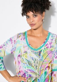 Färgglad, mönstrad tunika med V-ringning, trekvartsärmar och turkosa detaljer. Har palmlövsdesign i lila, gröna och blå nyanser.