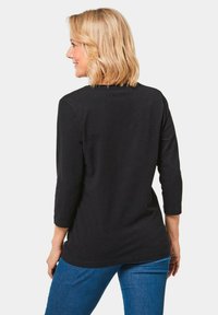 Zwarte, langemouwen shirt van zachte stof, met een ronde halslijn en een relaxte pasvorm, gecombineerd met blauwe denim jeans.