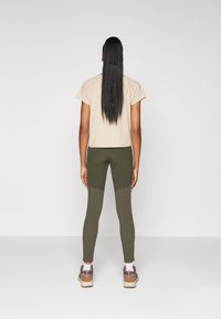 Beige cropped t-shirt, olive green leggings with textured panels, and gray and brown sneakers. Hair is long and straight.
