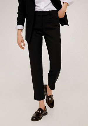 Black tailored ankle-length pants paired with black loafers, white shirt, and black blazer with rolled-up sleeves.