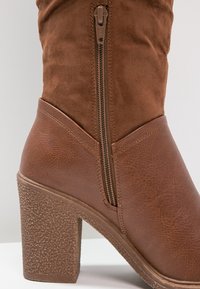 Bottine marron en similicuir texturé, avec talon bloc et fermeture éclair latérale. Tige lisse avec surpiqûres contrastantes.