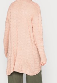 Ljusrosa stickad cardigan med ett texturerat mönster, ribbade manschetter och en avslappnad passform. Har en böjd söm och långa ärmar.
