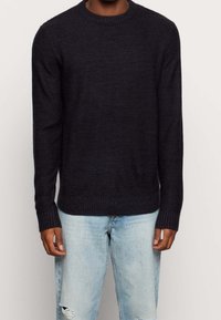 Marinblå ribbstickad tröja med rund halsringning och långa ärmar. Kombinerad med ljusblå slitna jeans, som visar en avslappnad passform.